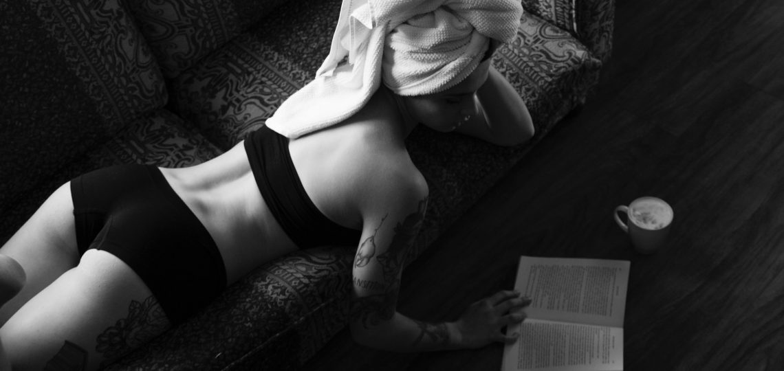 Femme en sous-vêtement allongée à plat ventre et lisant un livre.