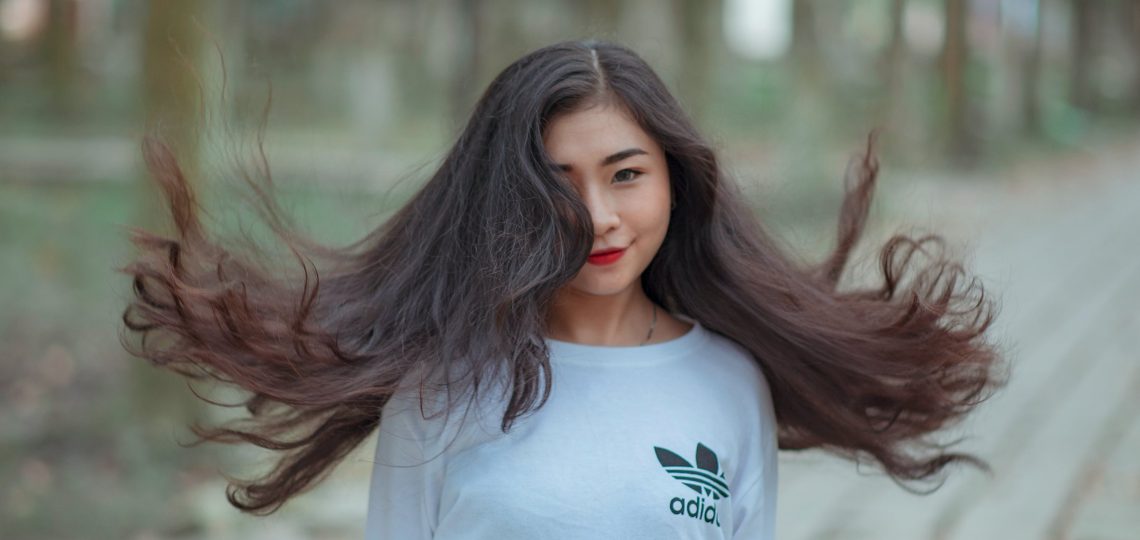 Une femme brune d'origine asiatique ayant les cheveux longs portant un sweatshirt d'une célèbre marque sportive.